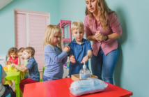 Young teacher at the preschool shows children how to use sanitazer and clean their hands. New hygienic rules at the kindergartens and schools to teach children to protect their health. New normal.