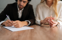 Cropped shot of spouses couple signing decree papers getting divorced in lawyers office at desk. Unhappy married family split break up end relationships giving permission to marriage dissolution.